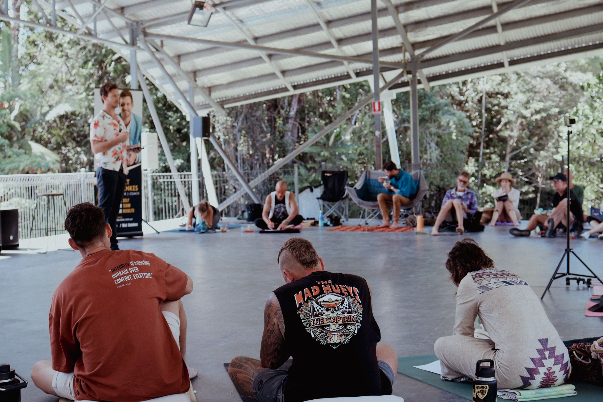 Mat Bankes speaking into a microphone at Connect Fest while the audience listens from mats on the floor